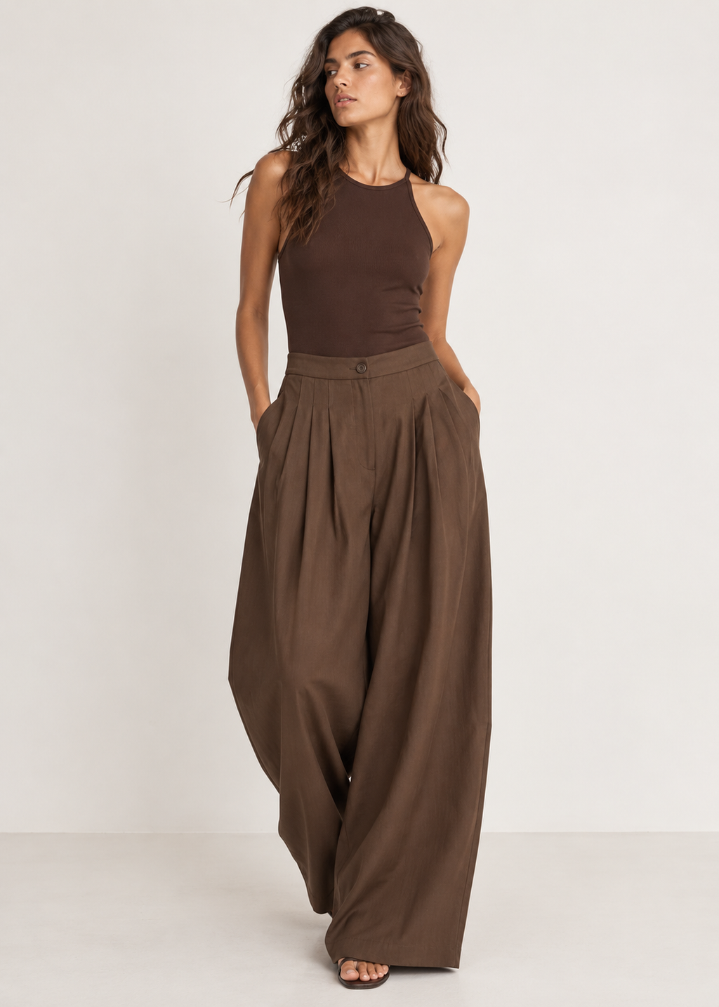 Front view of brown wide-leg trousers with a button waistband, deep pleats and side pockets