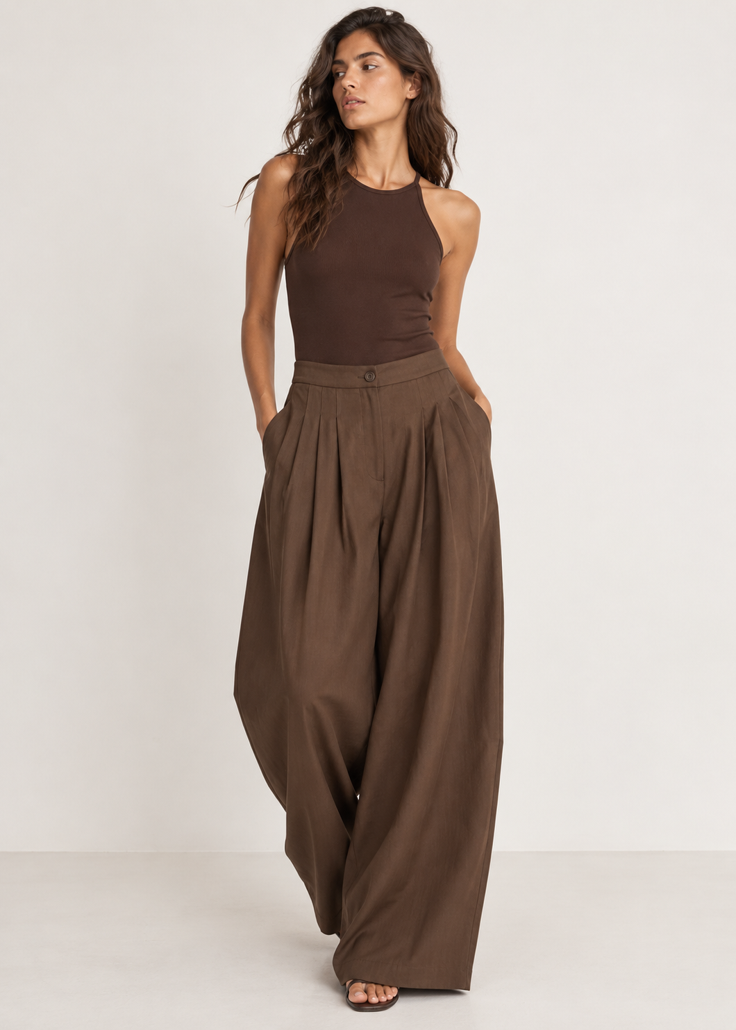 Front view of brown wide-leg trousers with a button waistband, deep pleats and side pockets