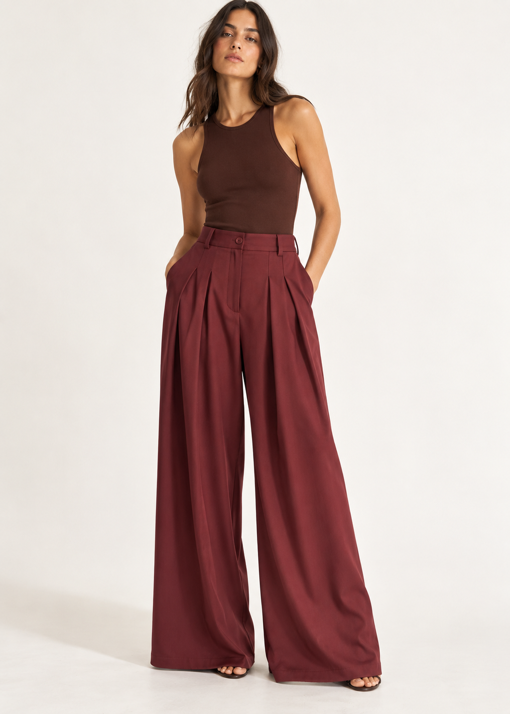 Model wearing burgundy pleated wide-leg trousers with a fitted sleeveless top