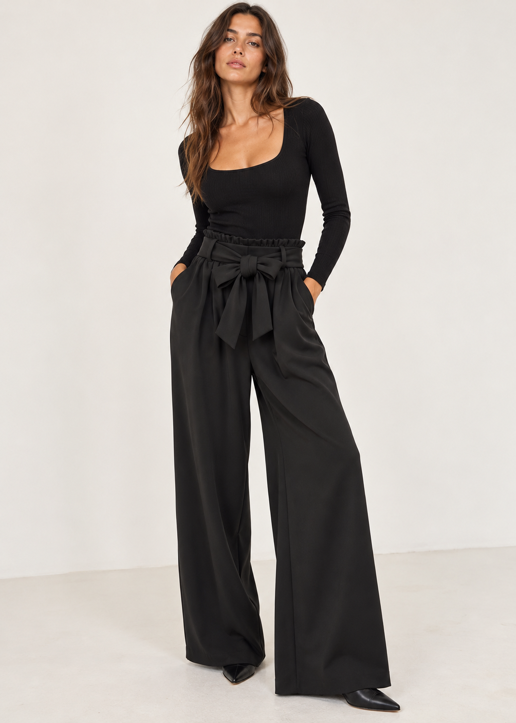 Model wearing black tie-waist paperbag palazzo trousers with a fitted black top and pointed shoes