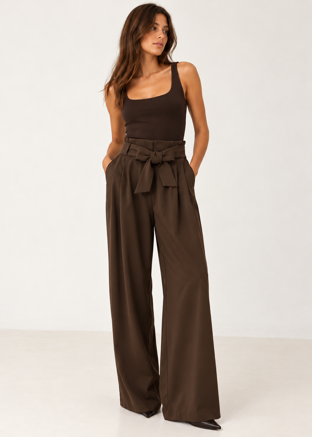 Model wearing chocolate brown tie-waist wide-leg trousers with a fitted dark tank and pointed shoes