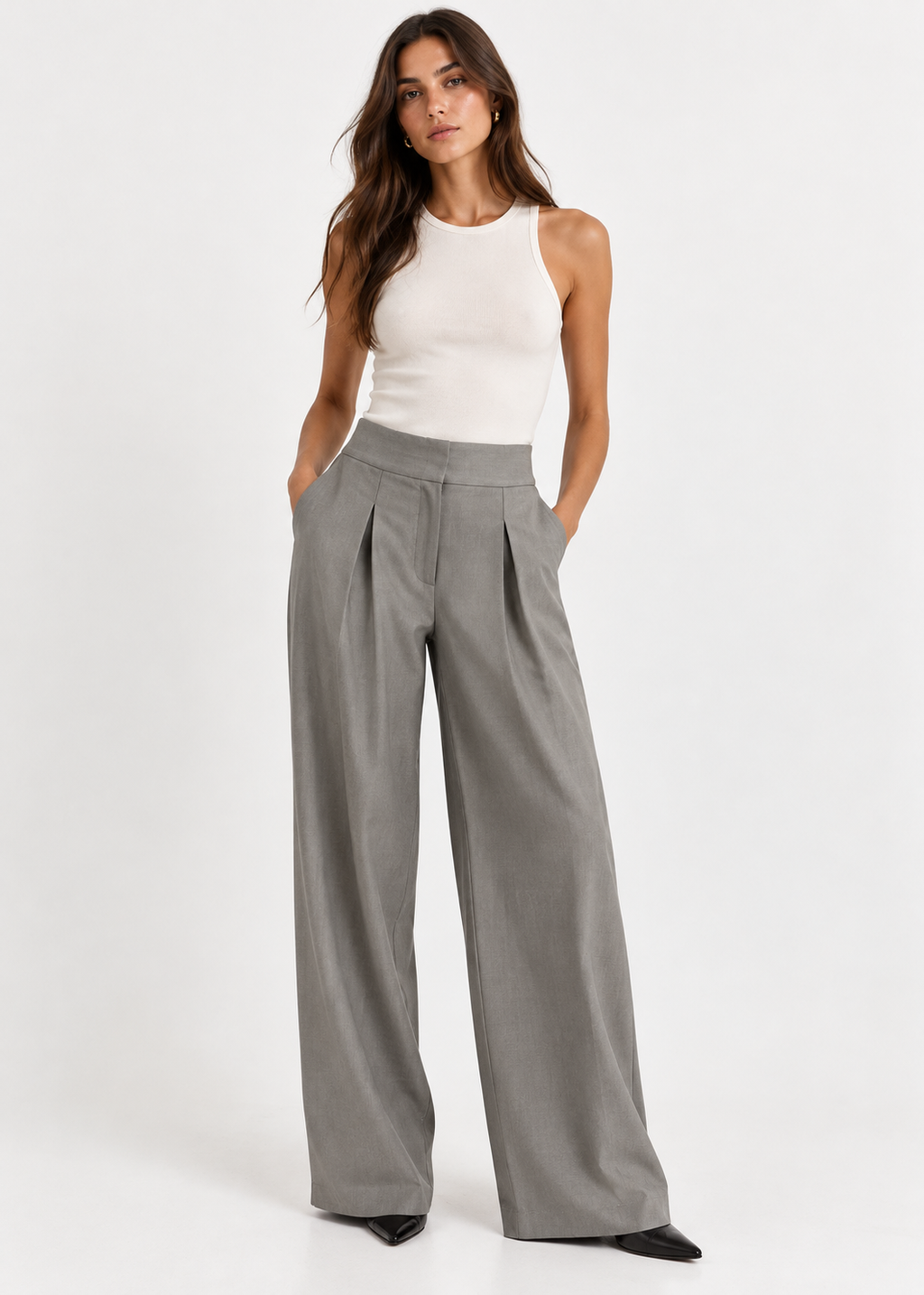 Model wearing grey-green pleated wide-leg trousers with a white tank top and black pointed shoes