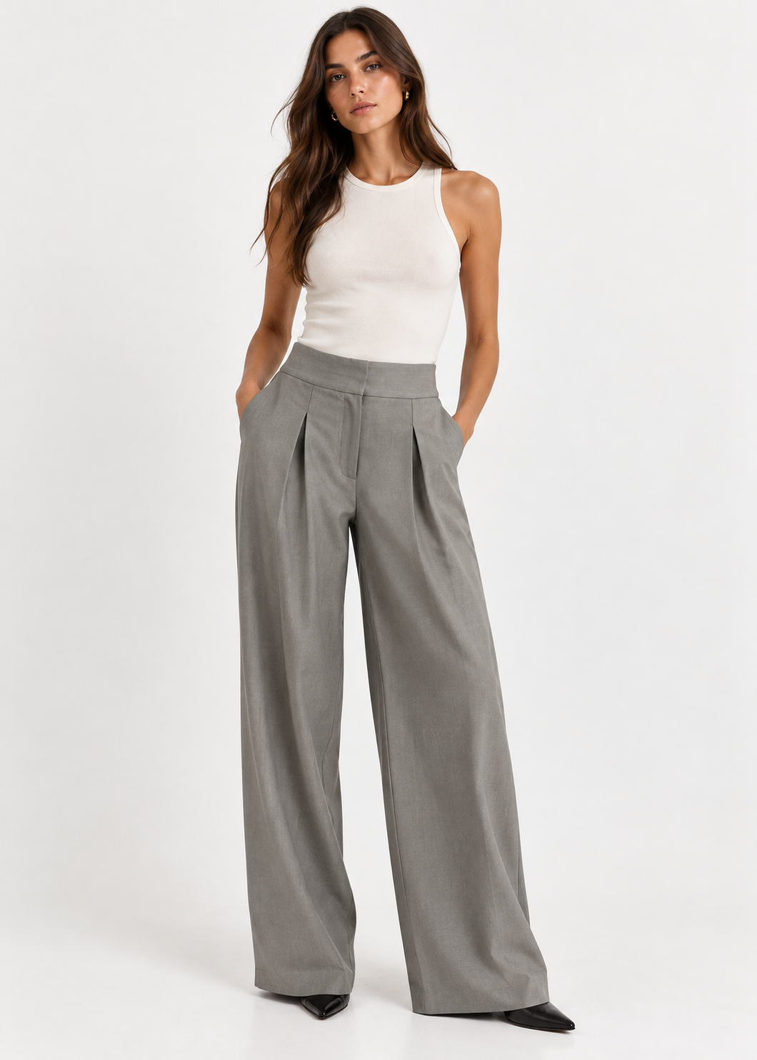 Model wearing grey-green pleated wide-leg trousers with a white tank top and black pointed shoes