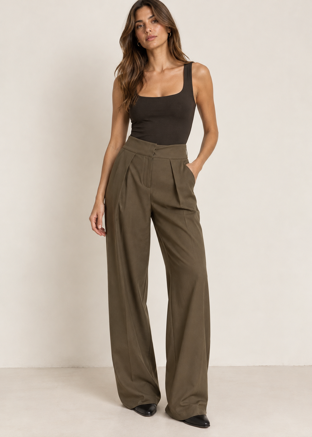 Model wearing olive high-waisted pleated wide-leg trousers with a dark fitted tank and black pointed shoes