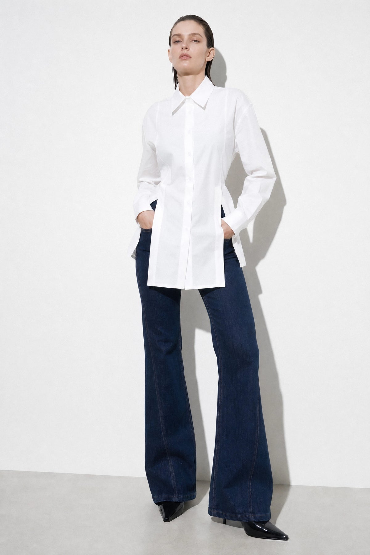 Model wearing a white longline shirt with dark wide-leg trousers