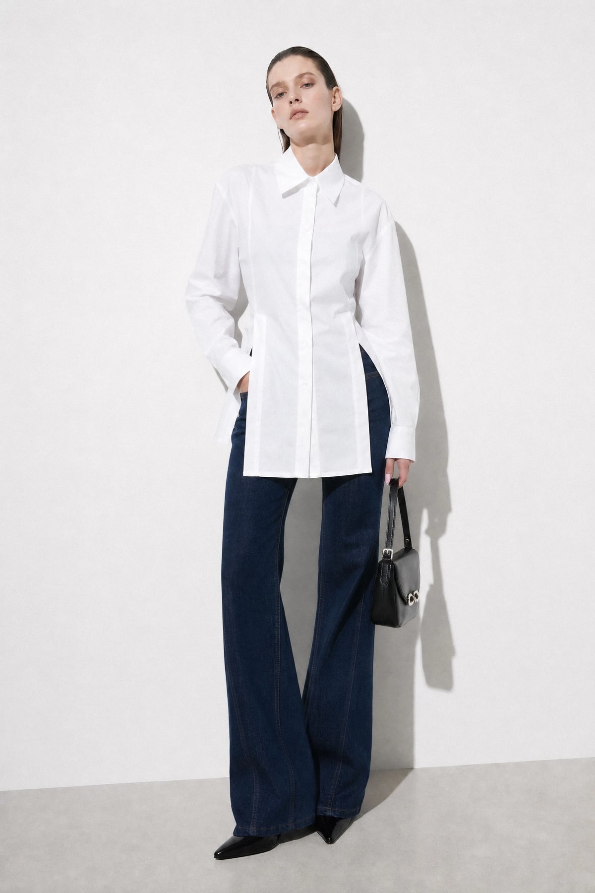 Model wearing a white fitted back-tie shirt with dark trousers and a black handbag
